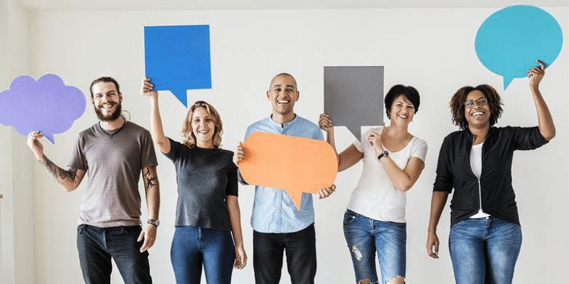 Foto de equipe de trabalho com 5 profissionais segurando nas mãos balões de fala de diversas cores
