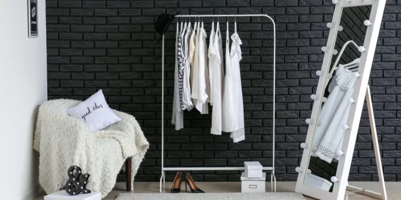 Foto de camarim para artistas com arara de roupas, poltrona e espelho em cores claras